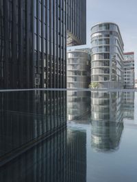 black building reflecting off the water on the edge of a city canal with a man and woman