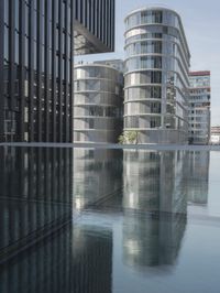 black building reflecting off the water on the edge of a city canal with a man and woman
