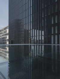 black building reflecting off the water on the edge of a city canal with a man and woman