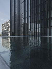 black building reflecting off the water on the edge of a city canal with a man and woman