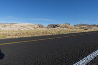 a black car driving along the road in a desert near mountains and dirt fields by itself