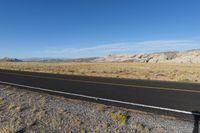 a black car driving along the road in a desert near mountains and dirt fields by itself