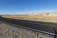 a black car driving along the road in a desert near mountains and dirt fields by itself