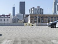 a black car parked on the concrete road in front of a cityscape in a parking lot