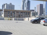 a black car parked on the concrete road in front of a cityscape in a parking lot