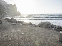 a black dog lying on top of a beach next to the ocean on top of rocks