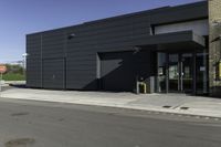 the entrance to an industrial building with a black door and glass door is beside a parking lot with trees