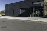 the entrance to an industrial building with a black door and glass door is beside a parking lot with trees