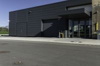 the entrance to an industrial building with a black door and glass door is beside a parking lot with trees