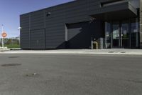 the entrance to an industrial building with a black door and glass door is beside a parking lot with trees