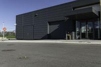 the entrance to an industrial building with a black door and glass door is beside a parking lot with trees