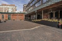 black potted planters sitting on the brick walkway outside a restaurant with tall buildings in the background