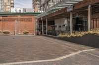 black potted planters sitting on the brick walkway outside a restaurant with tall buildings in the background