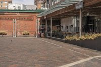 black potted planters sitting on the brick walkway outside a restaurant with tall buildings in the background