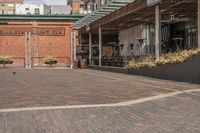 black potted planters sitting on the brick walkway outside a restaurant with tall buildings in the background