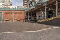 black potted planters sitting on the brick walkway outside a restaurant with tall buildings in the background