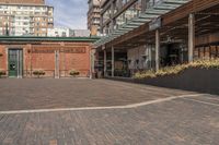 black potted planters sitting on the brick walkway outside a restaurant with tall buildings in the background