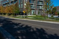 a black road next to an apartment building with grass and trees in front of it