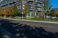 a black road next to an apartment building with grass and trees in front of it