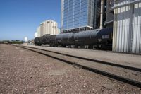 black train cars with steel rails and buildings in the background and on ground with no trees