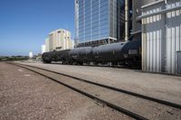 black train cars with steel rails and buildings in the background and on ground with no trees