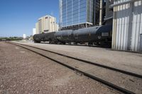 black train cars with steel rails and buildings in the background and on ground with no trees