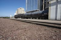 black train cars with steel rails and buildings in the background and on ground with no trees