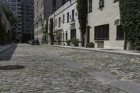 the cobblestone street has many stone sidewalks in front of it, where cars are parked and there is an outside bench with no visible