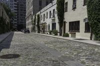 the cobblestone street has many stone sidewalks in front of it, where cars are parked and there is an outside bench with no visible