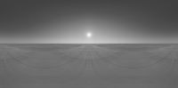 a black and white image of the sun on a snowy landscape with tracks in it