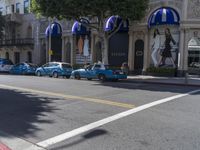 people are walking down the road near a store with blue and white awnings