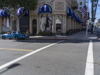 people are walking down the road near a store with blue and white awnings