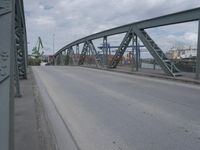 a blue train crossing a bridge over a river near buildings and a highway with no traffic