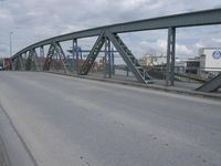 a blue train crossing a bridge over a river near buildings and a highway with no traffic