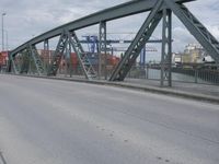 a blue train crossing a bridge over a river near buildings and a highway with no traffic