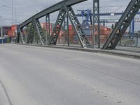 a blue train crossing a bridge over a river near buildings and a highway with no traffic