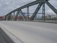 a blue train crossing a bridge over a river near buildings and a highway with no traffic