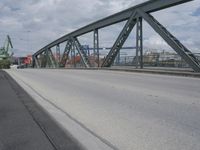 a blue train crossing a bridge over a river near buildings and a highway with no traffic