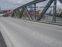 a blue train crossing a bridge over a river near buildings and a highway with no traffic