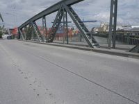 a blue train crossing a bridge over a river near buildings and a highway with no traffic