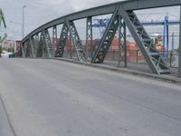 a blue train crossing a bridge over a river near buildings and a highway with no traffic