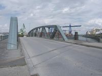 a blue train crossing a bridge over a river near buildings and a highway with no traffic