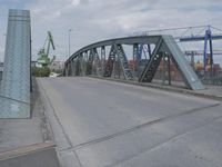 a blue train crossing a bridge over a river near buildings and a highway with no traffic
