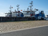 a row of blue tugsboats docked next to each other on a stone path outside