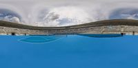 a tennis court is covered in blue water with a sky background and clouds above it