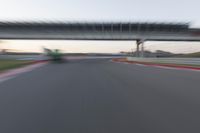 a blurry photo of a car driving on a racetrack by an overpass in the distance