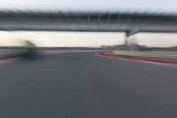 a blurry photo of a car driving on a racetrack by an overpass in the distance