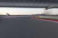 a blurry photo of a car driving on a racetrack by an overpass in the distance