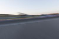 a blurry photo of a motorcycle racing down a racetrack with an airplane in the background