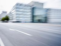 blurred picture of a street with cars driving past buildings in the background and an empty street
